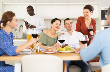 Multiethnic women and men friends talking and drinking wine in the kitchen