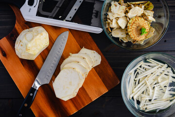 Peeled, Sliced, and Julienned Celery Root: Thin slices of celeriac on a wooden cutting board to be...