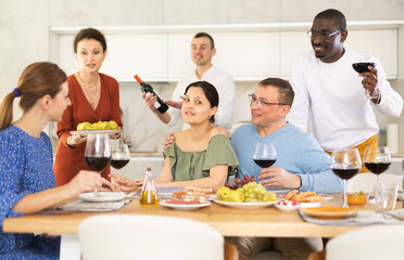 Multicultural female and male friends chatting and drinking wine at table