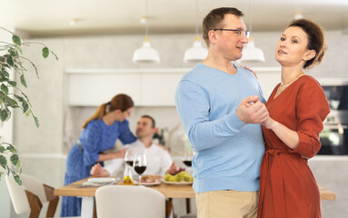 Obraz premium Positive woman in terracotta dress tenderly embracing man, enjoying slow dance at cozy friendly house party..