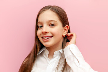 cheerful teenage girl in a white shirt and braces smiles and straightens her hair on a pink isolated background
