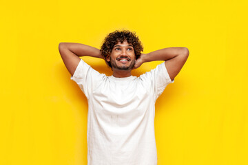 young cheerful indian man in a white t-shirt resting thinking and dreaming on a yellow isolated...