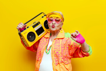 funny crazy granny in hipster clothes listening to music on a tape recorder and showing a kiss on a...