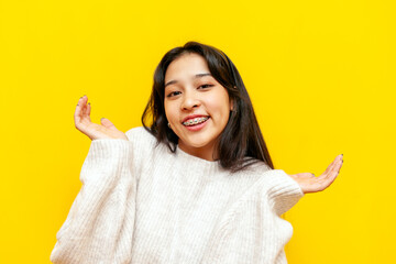 young unsure asian woman with braces shrugs over yellow isolated background, korean girl doesn't...