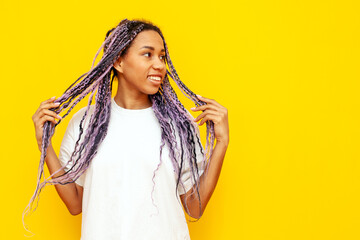 young african american woman with hipster colored dreadlocks smiling and holding her hair on yellow...