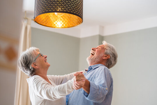 Joyful active old retired romantic couple dancing laughing in living room, happy middle aged wife and elder husband having fun at home, smiling senior family grandparents relaxing bonding together. - Powered by Adobe