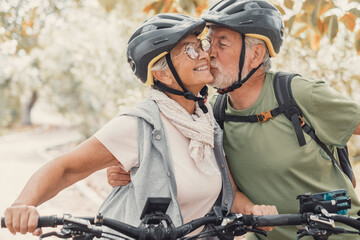 Couple of cute and sweet seniors in love enjoying together nature outdoors having fun with bikes. Old man kissing his wife smiling and feeling good..