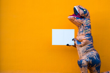 One happy and funny dinosaur costume dancing in the street with a orange colorful background - t-rex having fun - funny man inside of a costume of dino. © Daniel