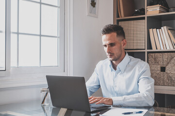 Happy young caucasian millennial businessman working at home at desk with laptop or computer having...