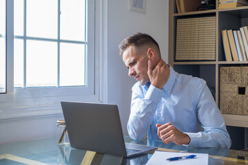 Pinched nerves, tensed sore muscles, fibromyalgia ache due sedentary lifestyle and incorrect posture concept. Caucasian ethnicity frowning man sitting at desk in front of laptop, touch neck feels pain