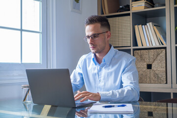 Happy young caucasian millennial businessman working at home at desk with laptop or computer having...