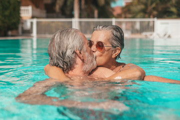 Couple of two happy seniors having fun and enjoying together in the swimming pool smiling and...