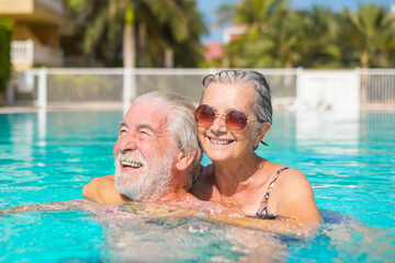 Couple of two happy seniors having fun and enjoying together in the swimming pool smiling and...
