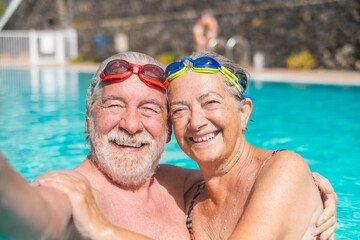 Couple of two happy seniors having fun and enjoying together in the swimming pool taking a selfie...