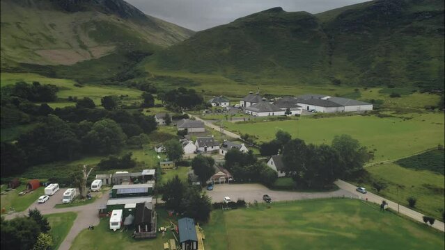 Scottish Arran whiskey distillery aerial view along road in greenery valley with mountains. Cottage, houses, camping in village. Epic summer scenery of Scotland's industy. Footage Shot