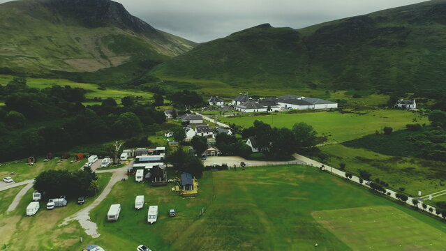 Scottish village aerial view: road, cottages, houses, distillery, camping in green valley at summer cloudy day. Picturesque mountains scenery from Arran Island, Scotland. Footage cinematic shot