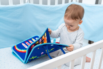 Baby playing with montessori busy book sitting in crib. Concept of smart books and modern toys