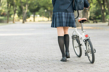公園の中を自転車を押して歩く制服姿の中学生・高校生・女子高生

