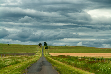 A country road in South East Queensland: picturesque journey beneath a dramatic sky, adorned with clouds, offering scenic beauty at every turn.