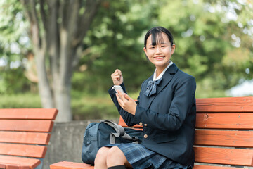 公園のベンチでスマホを持って喜ぶ女子中学生・女子高生（スマホデビュー・嬉しい・喜ぶ）
