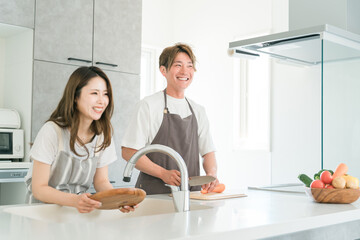 家のキッチンで一緒に料理を作る若いアジア人夫婦（お皿洗い・包丁）
