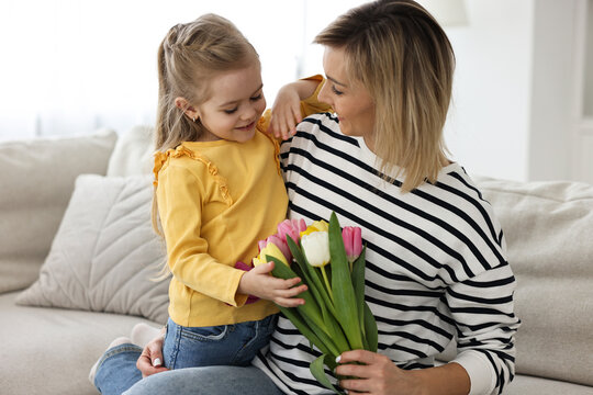 Little daughter congratulating her mom with Mother`s Day at home. Woman holding bouquet of beautiful tulips