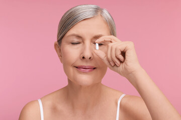 Beautiful woman with vitamin capsule on pink background