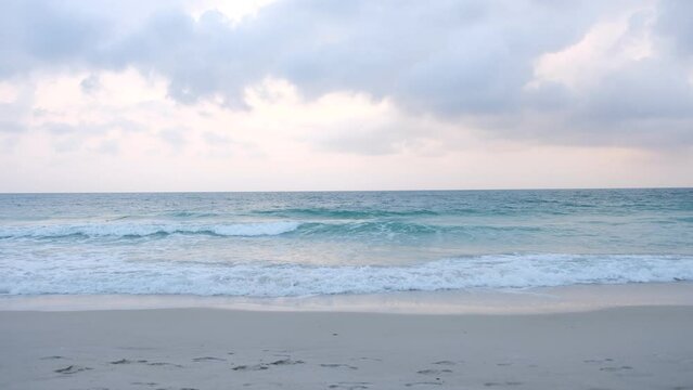 The sea has slight waves crashing on the sand and the sky was covered with white clouds.