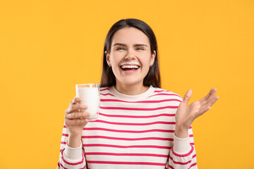 Happy woman with milk mustache holding glass of tasty dairy drink on yellow background