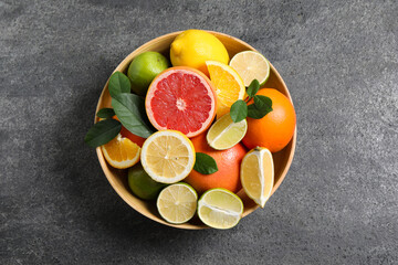 Different fresh citrus fruits and leaves in bowl on grey textured table, top view