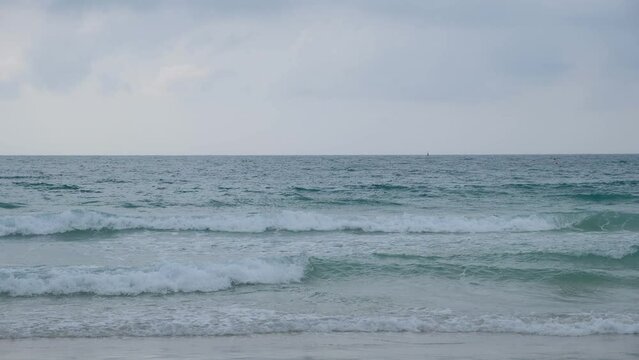 Beautiful blue ocean waves roll onto the brown sand beach.