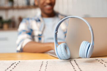 Closeup, smiling African African man using laptop, selective focus on wireless headphones