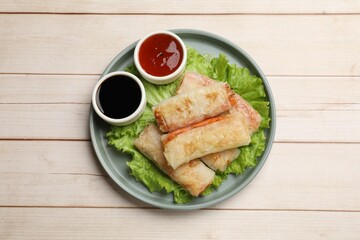 Delicious fried spring rolls and sauces on light wooden table, top view