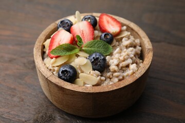 Tasty oatmeal with strawberries, blueberries and almond petals in bowl on wooden table, closeup