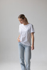 Beautiful blonde woman in a white T-shirt and blue jeans posing on a white background