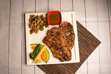 T Bone steak grilled meat with sauce, mushroom and salad served in dish isolated on napkin top view...