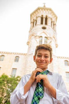 Portrait of a smiling boy tying a neck tie while standing outside of a church school building