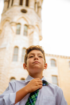 Portrait of a boy tying a neck tie while standing outside of a church school building