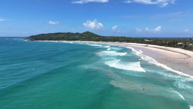 Drone slow-motion of the main beach of Byron Bay during the day with calm sea waves and blue sky