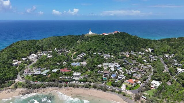 Drone of Wategos beach showcasing green cliff with buildings, lighthouse, sea and blue sky