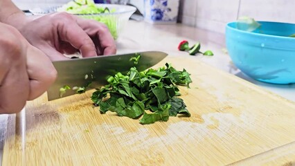 Caucasian hands cutting spinach leaves on bamboo cutting board at domestic kitchen, wide angle close-up with slow motion. Real life user-generated content.