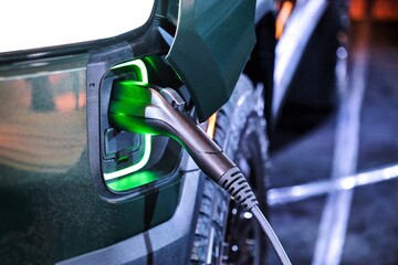 Close up of electric vehicle EV truck van charging on charging station with green power light...