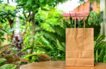 Paper shopping bag with blurred green garden background.Using Paper container for takeaway food or...