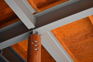 Large wooden beam bolted to steel girders supporting covered structure.