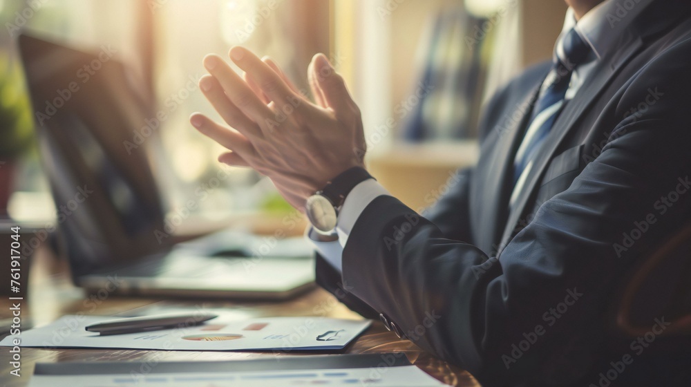 Poster a man in a suit is clapping his hands in front of a laptop and a stack of papers