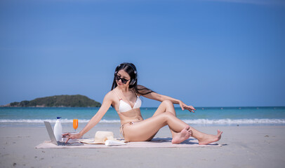 Happy sexy freelance woman wearing bikini sunglasses  workout relaxed drinking orange juice with work on laptop computer at beach in summer holidays.