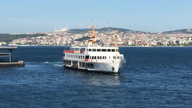 Tight view of a ferry transporting people across the Bosporus in Istanbul Turkey. The weather is beautiful, the sun is bright and the famous skyline is visible behind the large ship. 