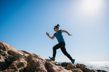 Woman runner running on sunrise seaside rocky mountains