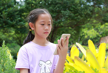 Portrait of Asian girl child looking smartphone screen while in park outdoor. Distant communication concept.