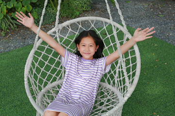 Portrait of happy Asian girl kid open hand wide while play on the white cradle or swing in the garden. - 761951431